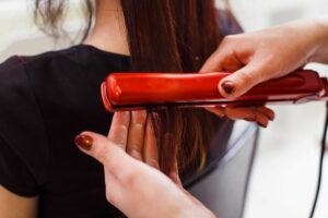 Mujer planchando cabello de un cliente con plancha de color rojo